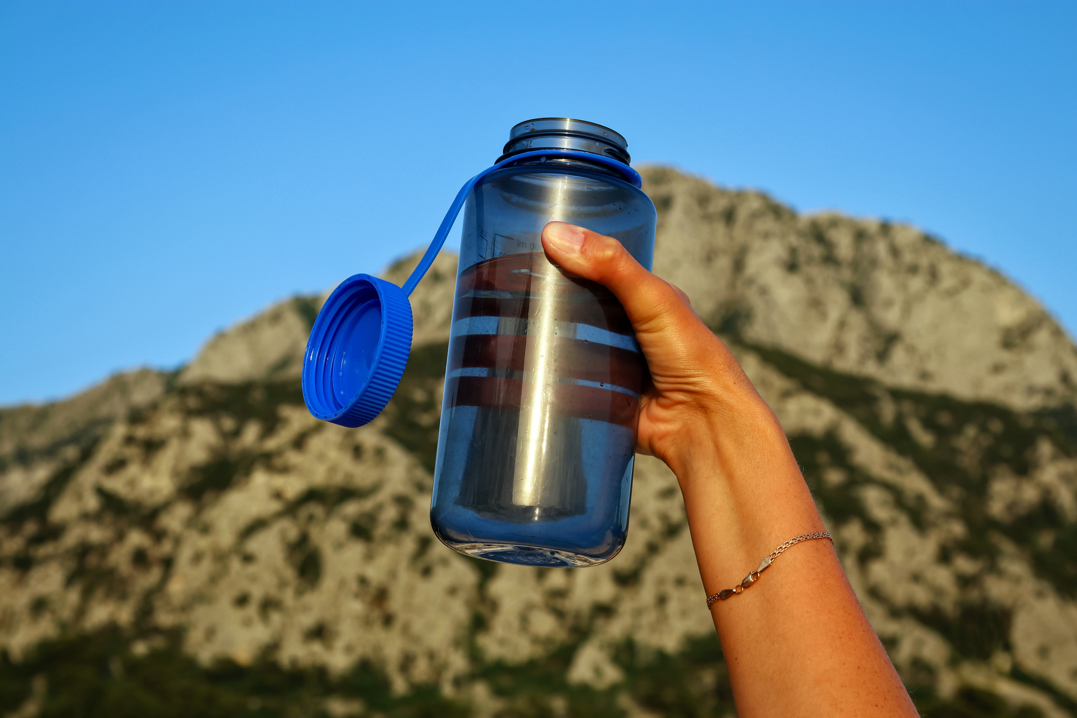 Tourist reusable blue bottle in a woman's hand on a mountain background